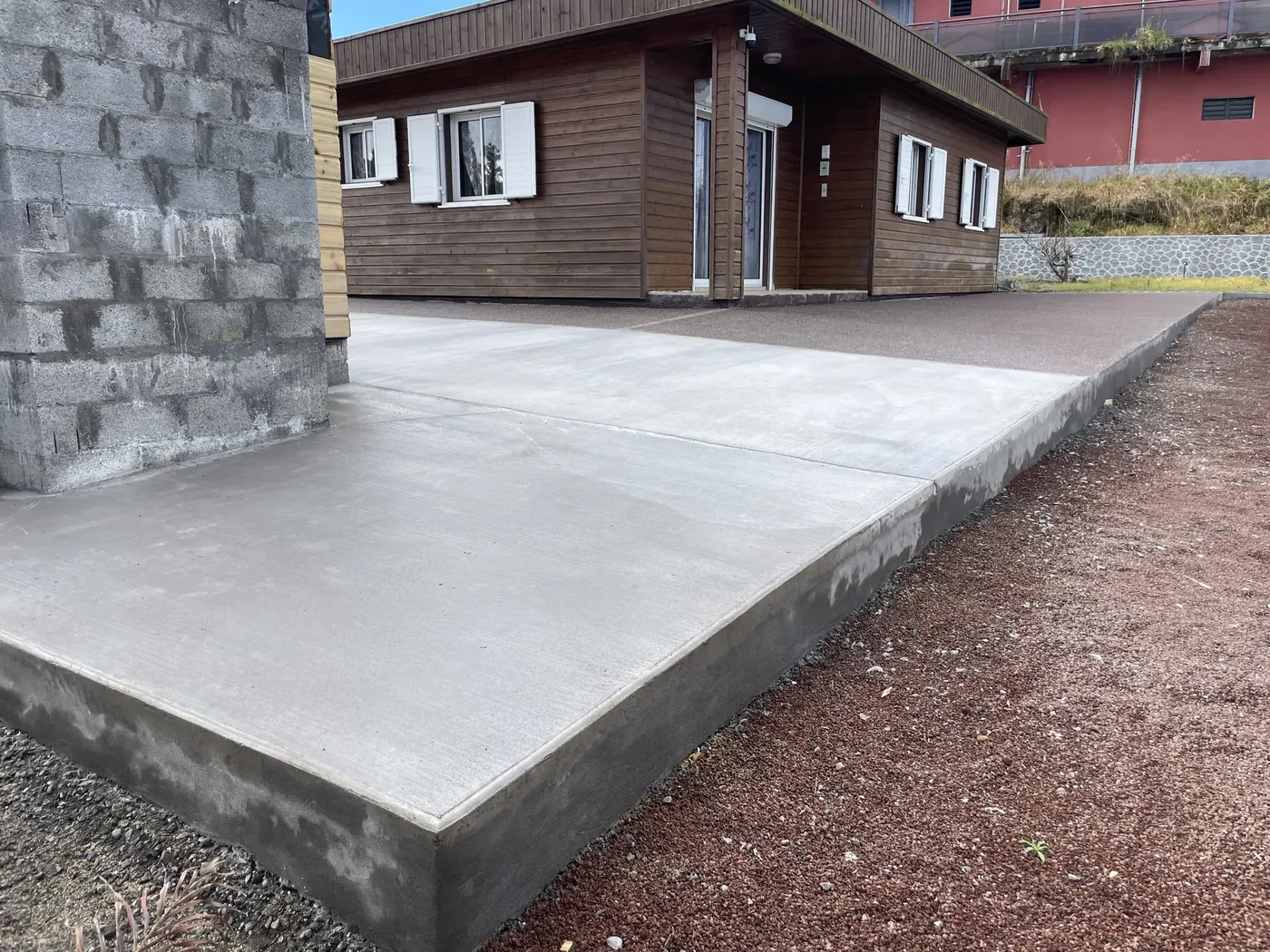 Dalle en béton balayé à bord relevé devant une maison en bois