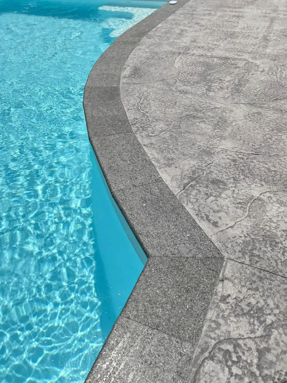 Détail d'une margelle anthracite et d'une plage de piscine en béton imprimé gris