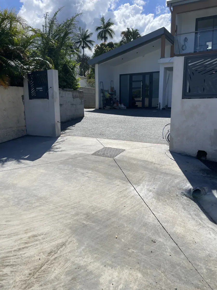 Cour bétonnée devant une villa, avec une bande de béton désactivé à l'approche du garage