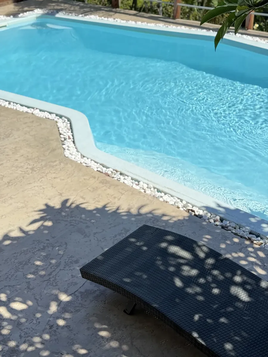 Plage de piscine en béton clair bordée de galets blancs
